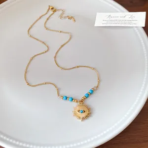 Detail view of golden stainless steel sun necklace with blue bead pendant on white plate