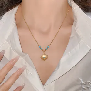 Detailed close-up of a gold sunburst necklace with a blue evil eye charm on a silk shirt.