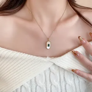 Close-up detail of a gold-plated necklace with shell inlay and green gem pendant