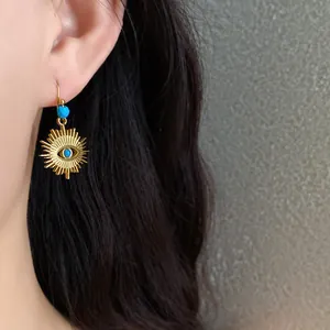 Detailed close-up view of a gold sunburst earring featuring an evil eye and blue bead.