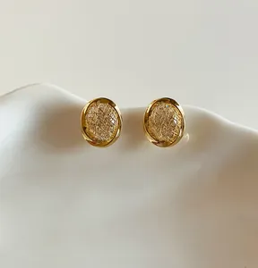 Detailed view of 18k gold plated zircon round ear clips on white ceramic tray