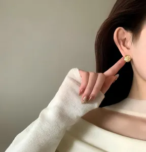 Close-up detail view of a minimalist textured 18k gold plated round ear clip worn by a model