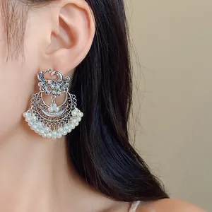 Detailed view of ethnic silver peacock earrings with white pearl tassels worn on ear model