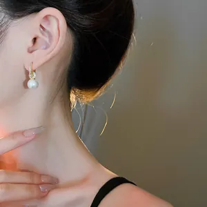 Elegante Goldohrringe mit weißen Perlen-Anhängern, Detailansicht am Ohr getragen.