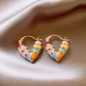 Close-up of colorful heart-shaped enamel hoop earrings displayed on champagne silk fabric