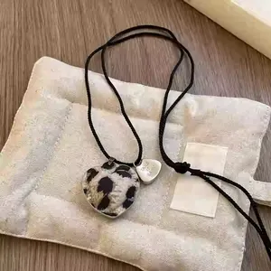 Close-up of leopard print heart necklace with 'Take it Easy' engraved charm on woven cord