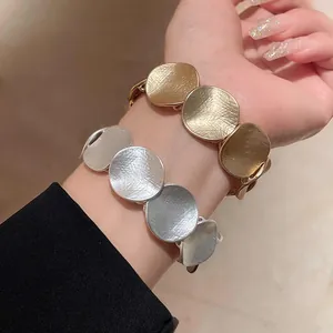 Detailansicht von strukturierten runden Metallarmbändern in Gold und Silber am Handgelenk.