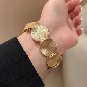 Nahaufnahme eines minimalistischen goldenen Armbands mit strukturierten Metallscheiben.