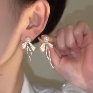 Dettaglio degli orecchini a fiocco con perle bianche e nappe di strass brillanti e lucidi