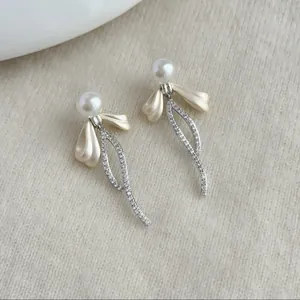 Dettaglio di eleganti orecchini a perla con fiocco e pendente curvo in cristalli.