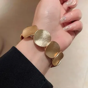 Nahaufnahme eines goldfarbenen strukturierten Metallplattenarmbands im minimalistischen Design