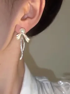 Dettaglio ravvicinato di orecchini a perno con fiocco in argento, perla e strass
