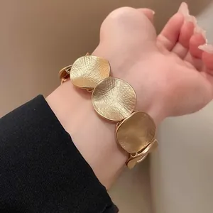 Detailansicht eines goldfarbenen runden Armbands mit Hammerschlag-Optik am Handgelenk