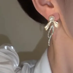Primo piano di eleganti orecchini a fiocco con perle e strass pendenti sull'orecchio