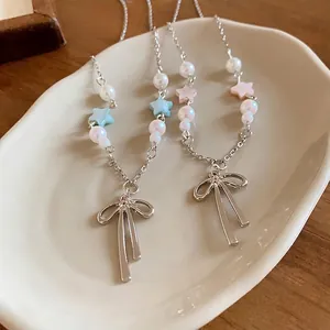 Elegant bow pendant necklace featuring white pearls and colorful star beads on a tray.