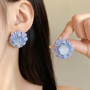 Close-up detail of sweet floral resin stud earrings with a light blue round stone worn on ear.