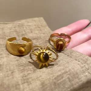Primo piano di tre anelli vintage color oro con pietre occhio di tigre su tessuto