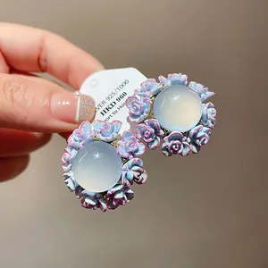 Close-up detail of floral resin stud earrings with blue-pink petals and clear center.