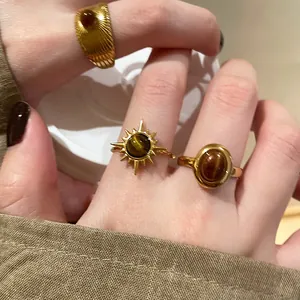 Dettaglio di anelli retrò color oro con pietre occhio di tigre artificiali sulla mano.