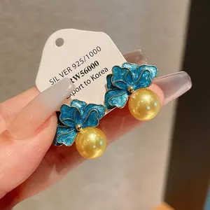 Dettaglio di orecchini a fiore in smalto blu con perle dorate e targhetta in argento