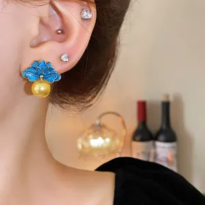 Primo piano di eleganti orecchini vintage a fiore in smalto blu con perle dorate sull'orecchio.