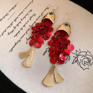 Close-up of red koi fish drop earrings with golden scales and shell tassel tail.