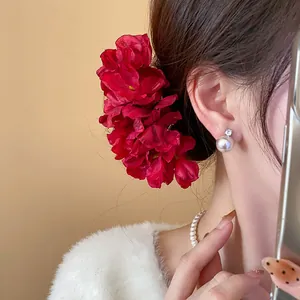 Detailed view of an elegant red fabric flower hair pin worn by a model in a sweet style