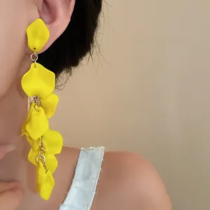 Detailed view of long exaggerated yellow flower petal tassel earrings worn on model.