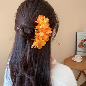 A detailed view showing an elegant orange fabric flower hair fork worn on a brunette bun.