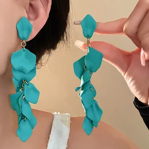 Close-up detail of oversized turquoise matte floral tassel earrings with a tiered petal design.