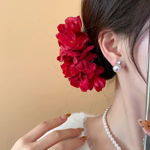 Close-up of an elegant large red fabric flower hairpin accessory on a model's dark hair