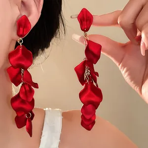 Detail view of long red pleated flower petal tassel earrings shown worn on a female model
