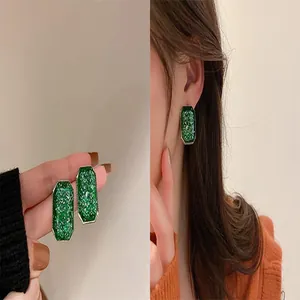 Elegant green rectangular earrings with glittery texture shown on model and in hand