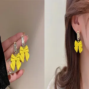 Detailed view of fashionable yellow bow earrings with crystals, shown worn and held in hand