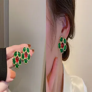 Vintage flower stud earrings with red and green crystals shown on model and in hand.