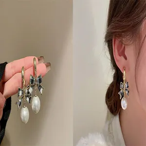 Elegant gold hoop earrings with black checkered bows and large white pearls shown worn on ear