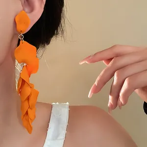 Close-up of vibrant orange long pleated petal tassel earrings on an Asian model.
