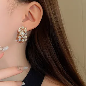 Primo piano di eleganti orecchini a lobo geometrici con perle e strass su modella