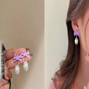Detailed macro view showing a stylish purple bow and white pearl drop earring worn by a model