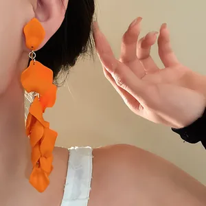 Close-up of exaggerated orange ruffled flower petal tassel long earrings on a model