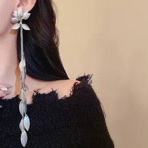 Primo piano dettagliato di un lungo orecchino a nappa d'argento con motivi di fiori e foglie.