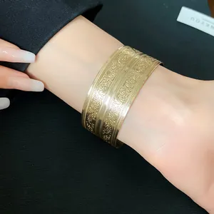 Nahaufnahme eines goldenen Armreifs im Vintage-Stil mit floralen Gravuren am Handgelenk.