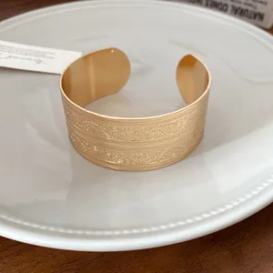 Detaillierte Nahaufnahme eines goldenen Metallarmreifs mit Gravur auf einem weißen Porzellanteller