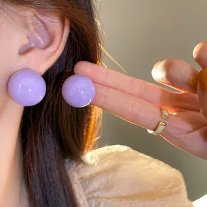 Primo piano di eleganti orecchini a lobo minimalisti a sfera viola lucida sull'orecchio