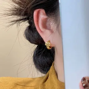 Primo piano di eleganti orecchini a cerchio in oro con fiori traforati indossati sull'orecchio