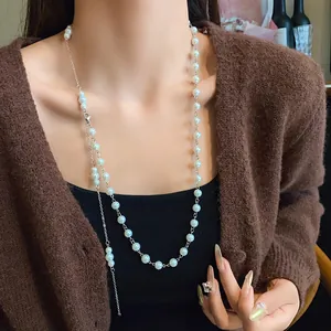Elegant French-style long pearl necklace worn as a sweater chain over a brown cardigan.