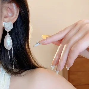 Primo piano di eleganti orecchini di perle a forma di rosa con nappe indossati da modella