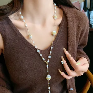 Close-up detail of irregular baroque pearls on a long gold-toned sweater chain necklace.