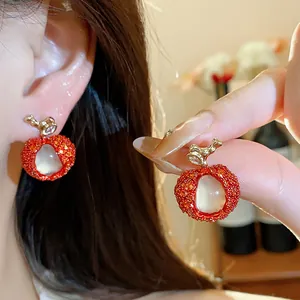 Detailed close-up of litchi shaped earrings featuring red zircon and white resin