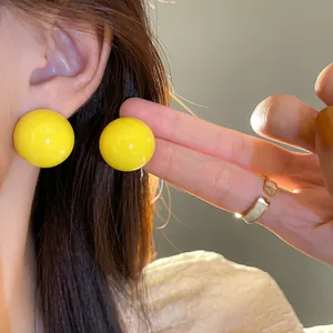 Dettaglio ravvicinato di orecchini a sfera gialla lucida e anello aperto dorato su modella